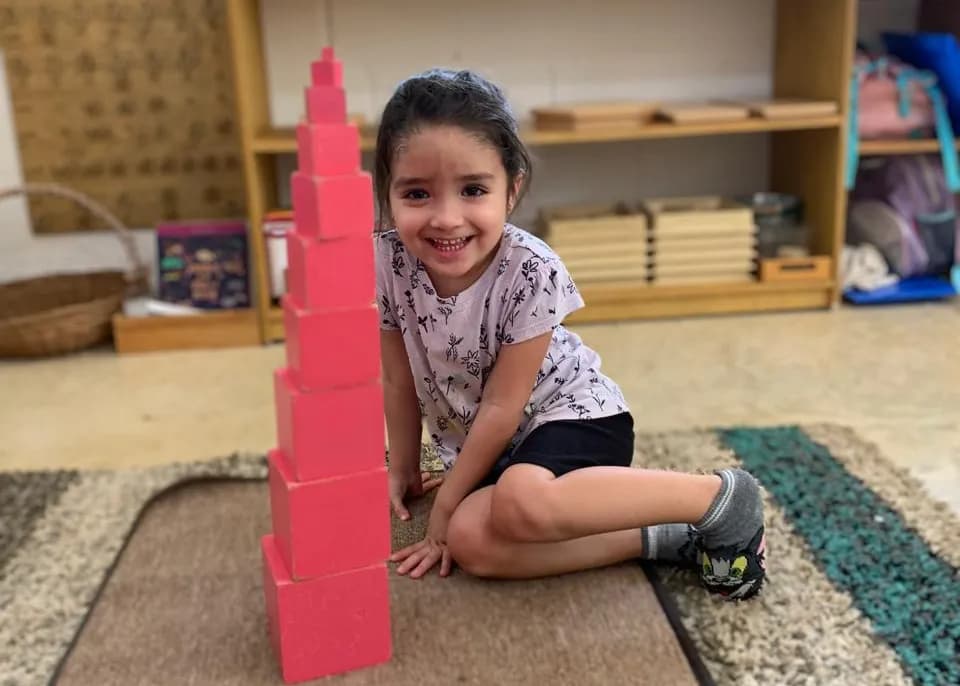 Niña sonriente junto a la torre rosa que acaba de construir