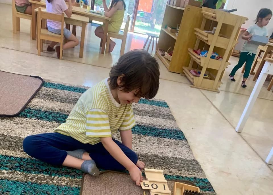 Niño trabajando con las tablas de Seguin en un ambiente Montessori, con otros niños al fondo