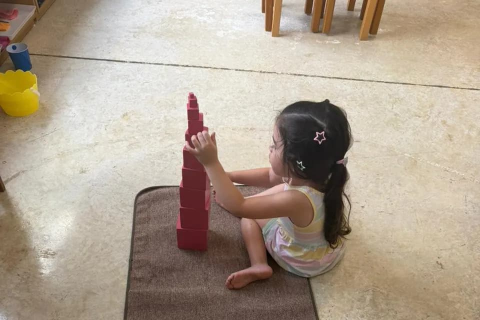 Niña concentrada construyendo la torre rosa en el suelo del ambiente